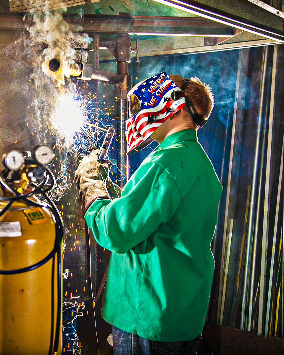 A student welder working in appropriate safety gear lighting up the scene with some sparks and smoke