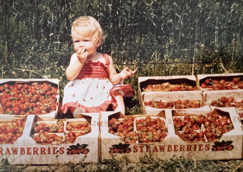 Melissa as a child holding strawberries on the family farm.